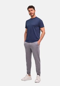 Navyblauwe katoenen t-shirt gecombineerd met grijze joggerbroek en witte sneakers. Het t-shirt heeft een ronde hals; de joggers hebben zijzakken.