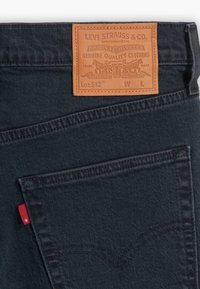 Poche arrière de jean en denim bleu foncé avec patch logo en cuir Levi Strauss et petite étiquette rouge en tissu sur la couture latérale gauche.