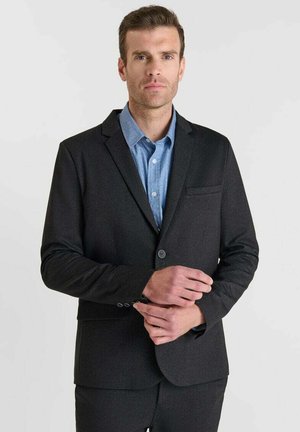 Blazer noir ajusté avec revers crantés, fermeture à un bouton et une poche poitrine, associé à une chemise col bleu clair.