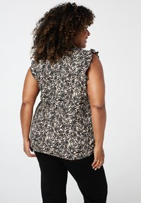Zwart en beige top met bladpatroon, met gerimpelde mouwen en een geplooide achterkant. Gecombineerd met zwarte broek. Gladde, lichte stof.