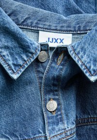 Denim shirt featuring a light blue fabric, pointed collar, double snap buttons with silver accents, and contrasting orange stitching.