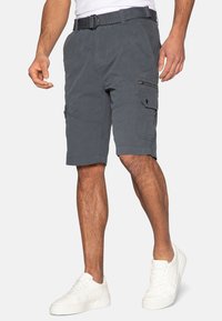 Pantalones cortos de cargo grises, hechos de un tejido de textura suave, que cuentan con múltiples bolsillos y un bolsillo con cremallera en el lado, combinados con zapatillas blancas.