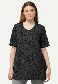 Top negro de manga corta con escote en V y un patrón floral en gris. Corte relajado con una textura suave y un ligero brillo. Combinado con jeans grises.