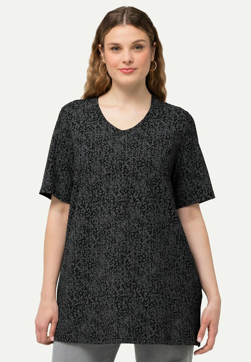 Top negro de manga corta con escote en V y un patrón floral en gris. Corte relajado con una textura suave y un ligero brillo. Combinado con jeans grises.