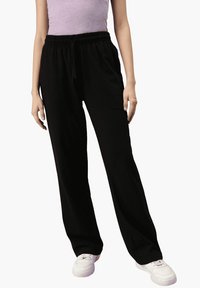 Schwarze Sweatpants mit einem elastischen Bund und Kordelzug, lockerer Schnitt und glatter Textur, kombiniert mit weißen Turnschuhen.