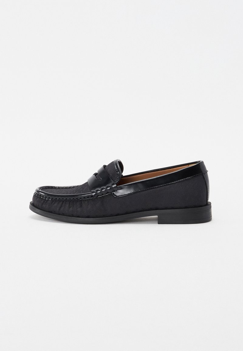 Mocassin noir pour homme avec garniture en cuir, couture moc toe et talon bas empilé, présenté en profil latéral sur fond blanc.