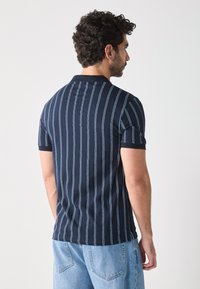 Polo shirt bleu marine avec des rayures verticales bleu clair, dotée d'un col et de manches courtes. Le tissu semble doux et texturé.
