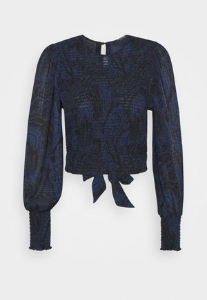 Navy blue cropped blouse with long puff sleeves, textured fabric featuring a subtle pattern, and a tied detail at the hem.