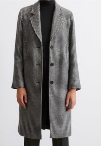 Abrigo de cuadros en blanco y negro con cuello, mangas largas, tres botones y un diseño de longitud media. Fabricado con una tela texturizada.