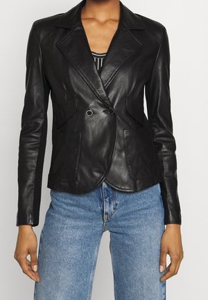 Vrouw die een zwarte leren dubbelreeksblazer draagt over een gestreepte top, gecombineerd met hoog getailleerde blauwe spijkerbroek, getoond vanaf halverwege het bovenbeen omhoog.