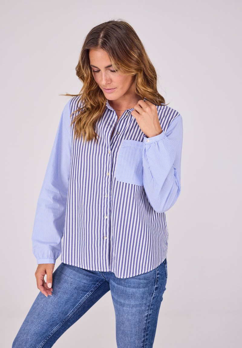Gestreiftes Button-Down-Hemd in Hellblau und Weiß mit langen Ärmeln, Stehkragen und einer einzelnen Brusttasche. Zusammengetragen mit blauen Jeans.