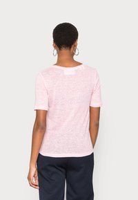 Light pink short-sleeve T-shirt made of a soft, slightly sheer fabric. Rounded neckline with a small back detail. Smooth texture and casual fit.