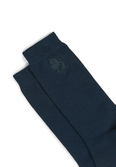 Chaussettes bleu foncé en matériau doux et texturé. Elles présentent un détail logo discret près de la cheville, avec un design côtelé classique.