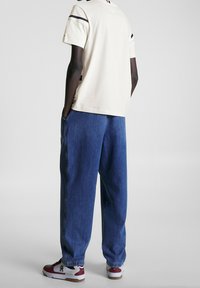 Camiseta de manga corta beige claro con rayas negras, combinada con pantalones vaqueros de denim azul holgados y zapatillas blancas con detalles rojos.