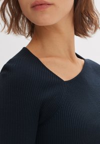 Top in maglia a coste navy con scollatura a V, caratterizzato da un design aderente e maniche corte, che mette in risalto un tessuto testurizzato per un ulteriore approfondimento.