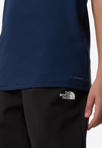 Μπλε σκούρο πουκάμισο με κοντά μανίκια από υφή υφάσματος, με ετικέτα FLASHDRY. Συνδυάζεται με μαύρο παντελόνι που φέρει λευκό λογότυπο.