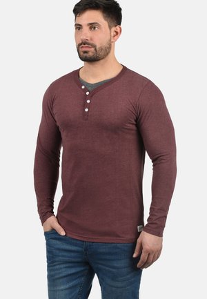 Bordeauxrot langärmliges Shirt mit Notch-Kragen, fünf Knöpfen und einem kontrastierenden grauen Innenkragen. Enganliegend.