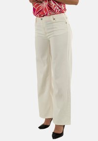 Jeans blancos de pierna ancha con una textura suave, que cuentan con cierre de cremallera y botón, bolsillos laterales y detalles de costura sutiles.