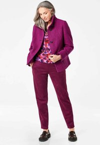 Fuchsia Wolljacke mit quiltierter Textur, rundem Kragen und schwarzen Knöpfen, kombiniert mit einem Musteroberteil und plüschfarbener, schmal geschnittener Hose.