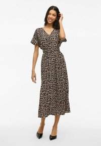 Robe à imprimé léopard en tissu léger, décolleté en V, manches courtes, taille cintrée et jupe fluide ; associée à des escarpins noirs à bout pointu.