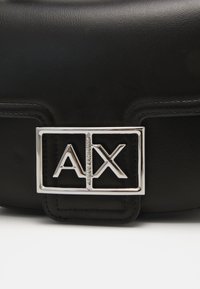 Borsa a tracolla in pelle nera con un evidente logo argentato "AX" e accessori rettangolari. Texture liscia con dettagli di cuciture precise.