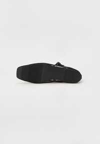 Chaussure noire avec une semelle en caoutchouc texturée, présentant un design élégant et une silhouette ouverte. Le matériau supérieur semble léger et flexible.