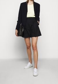 Marinblazer, lysegul top, høj talje sorte shorts og hvide sneakers. Sort bucket bag som accessory. Enkel og moderne design.