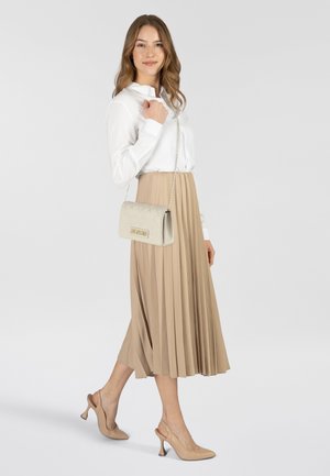 Sac en bandoulière matelassé couleur beige clair avec une chaîne et des détails en matériel doré, associé à une blouse blanche et une jupe plissée beige.
