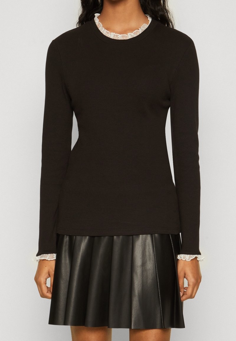 Svart långärmad topp i ribbat material med en vit volangkrage. Matchad med en svart plisserad läderkjol.