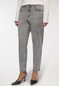 Jeans in denim grigio con design a gamba dritta, dotati di tasche frontali e una texture sbiadita. Abbinati a tacchi neri a punta.