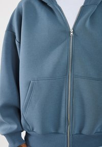 Blauwe rits hoodie van zacht materiaal, met een voetrits, kangoeroepockets en geribde mouwen en zoom. Soepele textuur, casual ontwerp.