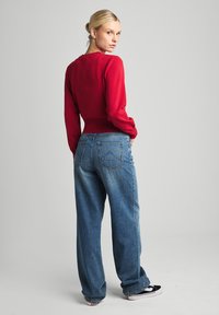 Pull en tricot rouge à manches longues, associé à un jean en denim bleu clair ample. Des baskets noir et blanc complètent la tenue.