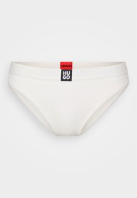 Un slip en coton blanc avec une texture côtelée. Présente une étiquette de logo noir et rouge sur la taille. Forme et design classiques.