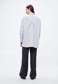 Svetlomodrá oversize košeľa s golierom na gombíky, záhybmi na chrbte a dlhými rukávmi. Kombinovaná s tmavými širokými džínsovými nohavicami.