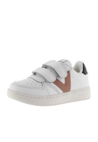 Sneaker bianco con tre strisce di velcro grigie, accento a V in suede marrone, punta perforata e dettaglio sul tallone blu navy. Suola in gomma.