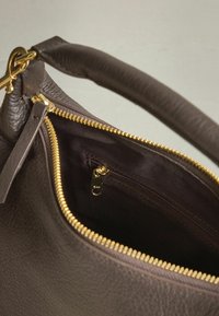 Ruskea nahkalaukku, jossa on kultainen vetoketju, sileä pinta ja sisätasku vetoketjulla. Kahva on myös nahkaa.