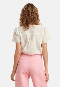 White eyelet blouse with short puff sleeves, featuring intricate patterns. Paired with light pink textured high-waisted trousers.