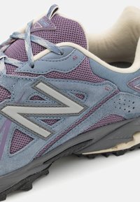 Scarpa da ginnastica con tomaia in mesh blu e viola, dettagli in suede grigio, grande logo "N" e suola in gomma nera testurizzata.