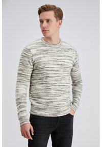 Pulover s kremno in sivo črtami, okroglim izrezom, rebrastimi manšetami in spodnjim robom, iz teksturiranega pletenega materiala, nošen s temnimi kavbojkami.