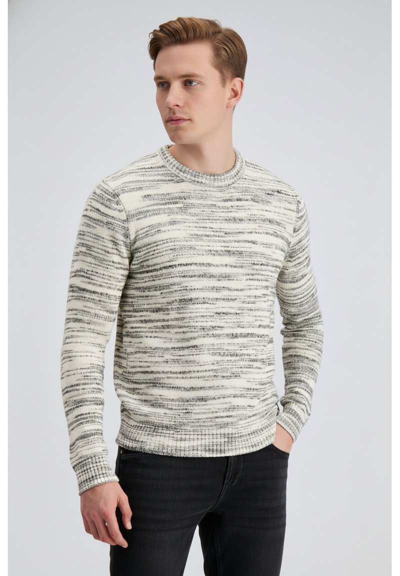 Pulover s kremno in sivo črtami, okroglim izrezom, rebrastimi manšetami in spodnjim robom, iz teksturiranega pletenega materiala, nošen s temnimi kavbojkami.