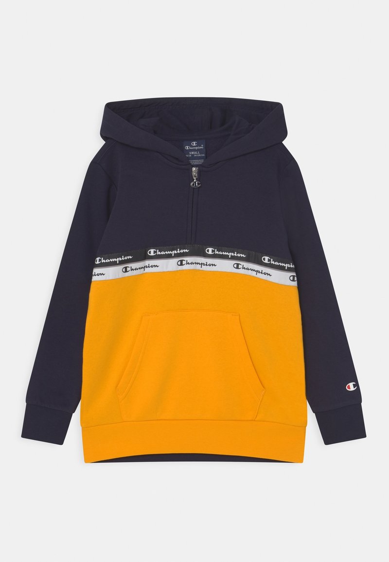 Sweat à capuche bleu marine et jaune avec poche avant, demi-fermeture éclair, bande avec logo Champion sur la poitrine, et petit logo sur le poignet de la manche gauche.