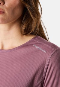 Violetti urheilupaita, jossa on tekstuuri-kuvio, pyöreä pääntie ja ommeltuja yksityiskohtia sekä "SWEDEMOUNT"-brändäys olkapäällä.