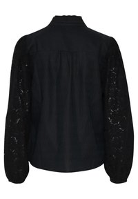 Blouse noire avec un col à volants, manches longues en dentelle texturée et un dos froncé. Tissu doux avec une légère brillance.