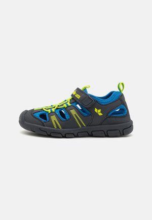 Sandal preto e azul com accents amarelos, apresentando um cabedal em malha respirável, tira ajustável e uma sola de borracha texturizada para melhor aderência.