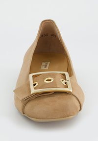 Ballerine en daim beige à bout rond, avec une boucle rectangulaire dorée et un nœud plissé en décoration à l'avant. Doublure intérieure lisse.