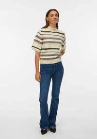 Suéter de manga corta de punto en color crema con rayas horizontales en lila claro y negro, combinado con vaqueros acampanados de color azul oscuro.