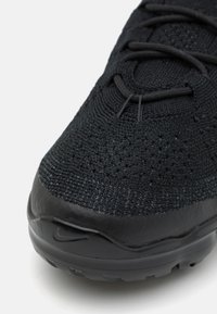 Black athletic shoe with a knit upper, textured finish, and a smooth black rubber sole. Features black laces and a subtle logo accent.