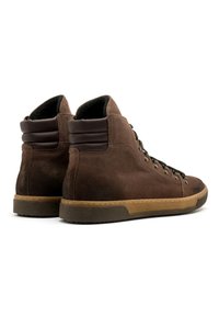 Brązowe zamszowe buty wysokie typu high-top o teksturowanej powierzchni, z kontrastującymi ciemnobrązowymi akcentami w okolicy kołnierza oraz gumową podeszwą ze szczegółami przeszycia.