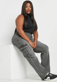 Pantalones cargo de denim gris desgastado con bolsillos laterales. Combinados con una camiseta sin mangas negra y zapatillas negras con detalles blancos.