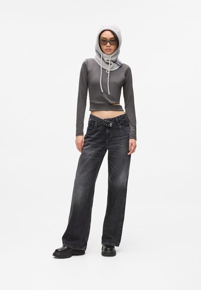 Haut gris à manches longues coupe courte avec une capuche à cordon de serrage, associé à un jean noir en denim ample et des chaussures noires chunky. Design simple avec des accents minimalistes.